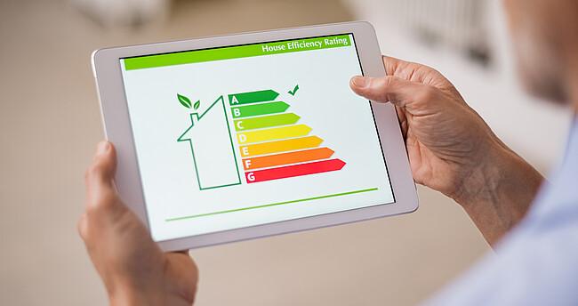Symbolbild Gebäudeenergieeffizienz; Ein Mann hat ein Tablet in der Hand, auf dem ein Gebäude mit Energielabel zu sehen ist.