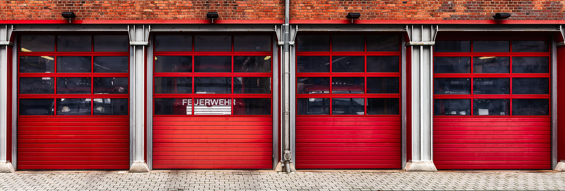Feuerwehrhaus Bild zeigt ein Feuerwehrhaus, hinter dessen Fenster ein Feuerwehrfahrzeugt steht