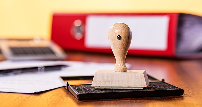 Schreibtisch mit Stempel und Büromaterial Stempelkissen mit Stempel und rotem Ordner im Hintergrund