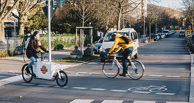 Bild zeigt 2 Fahrradfahrer beim Überqueren einer Straße Bild zeigt 2 Fahrradfahrer beim Überqueren einer Straße